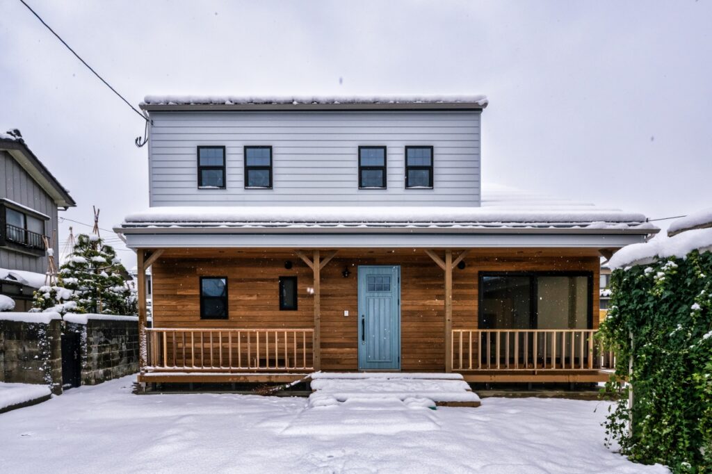 ポプラのベベルサイディングと造作手摺に囲まれたカバードポーチのある外観